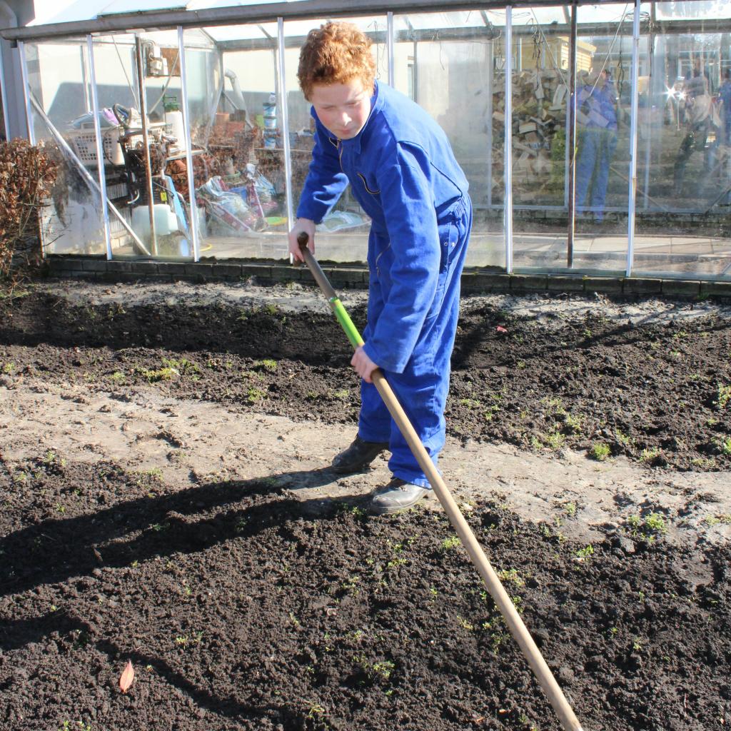 WP praktijkschool jongen buiten kas schoffel staand.JPG